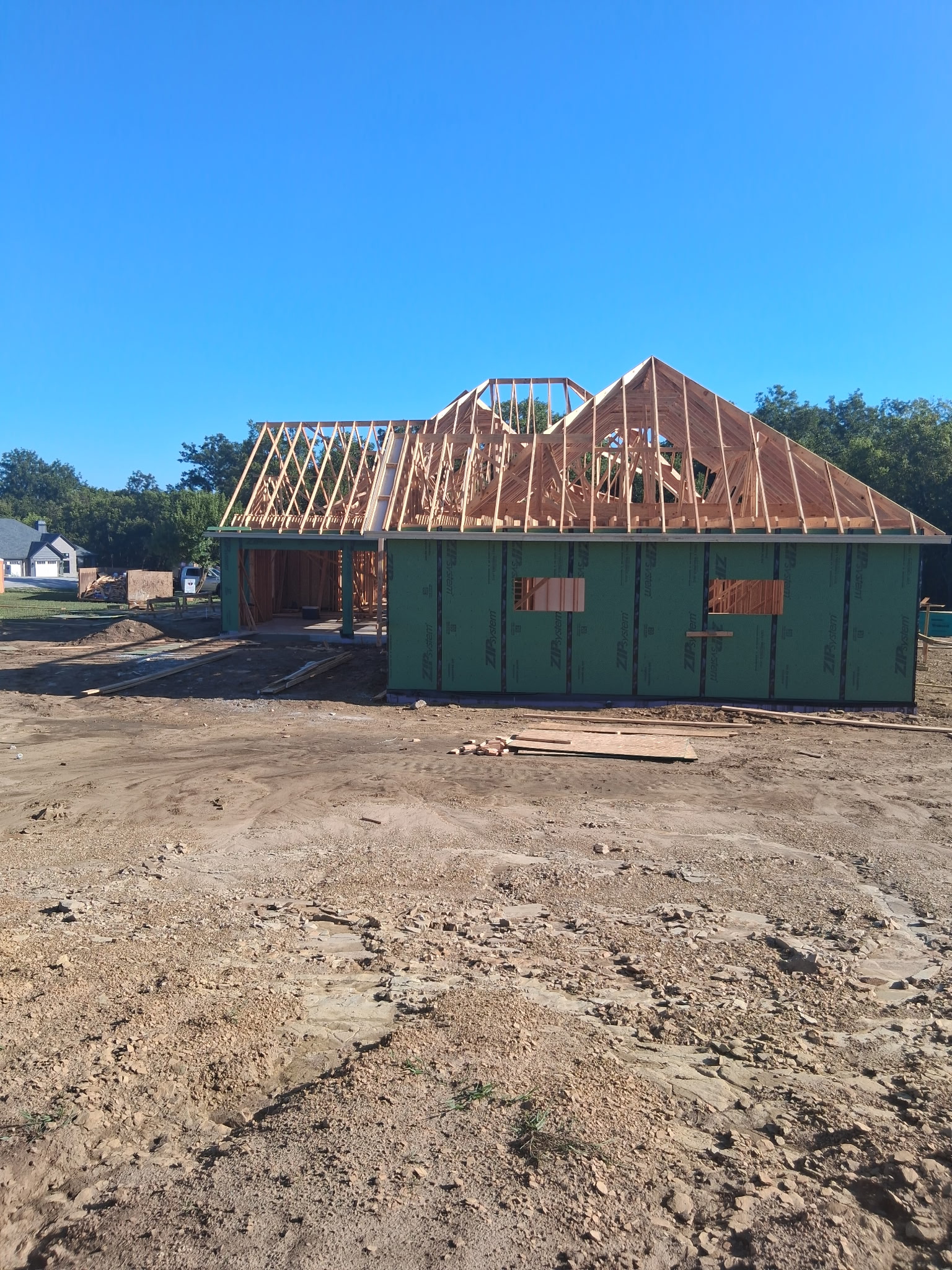 New residential home framed and wrapped, with roof trusses set against a clear sky