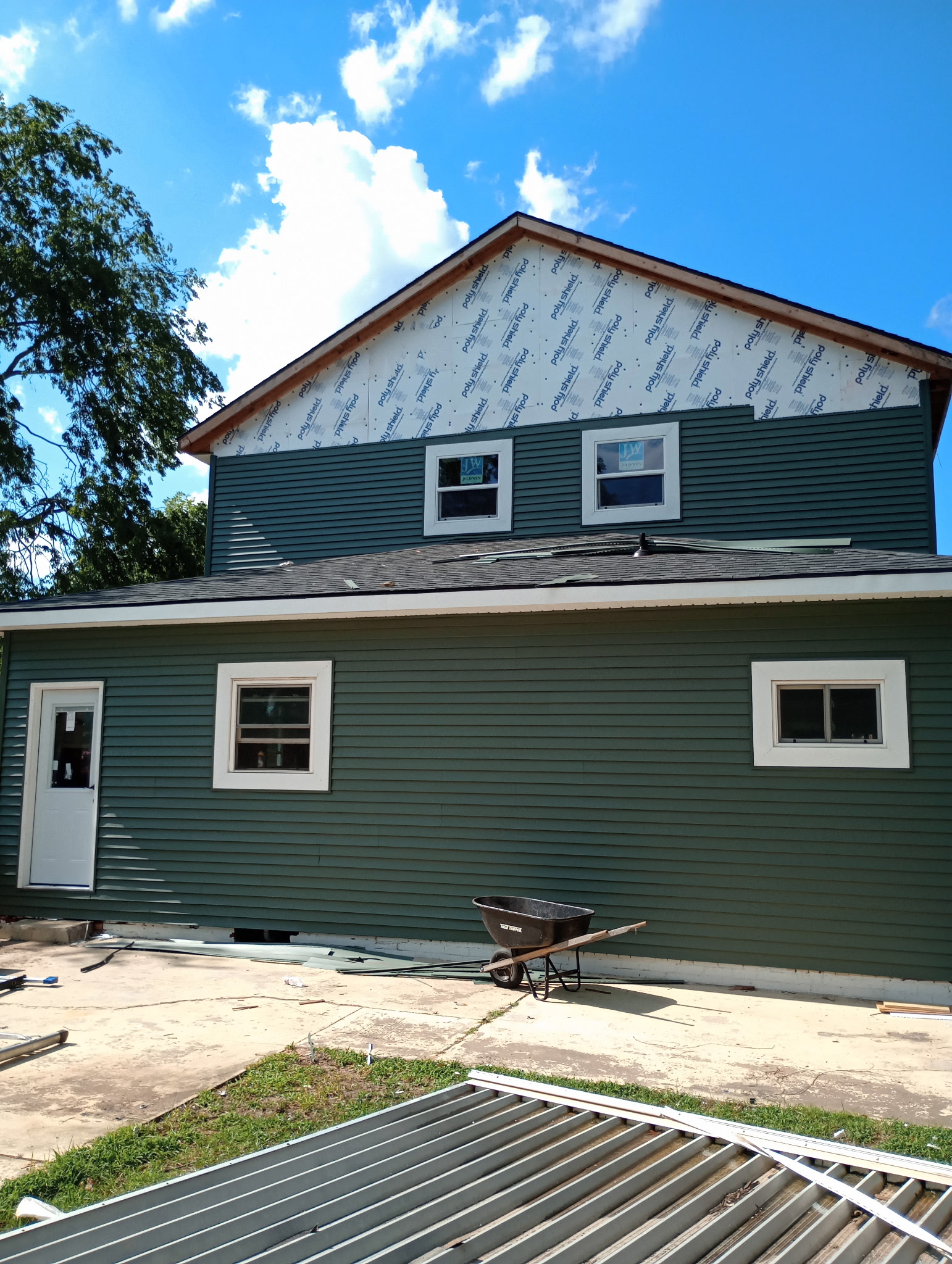 Two-story house with new siding, windows, and a shingle roof during exterior work