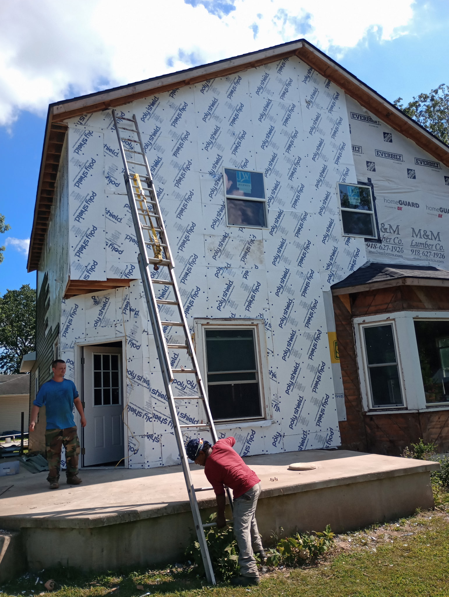 Two-story house wrapped for exterior work, with new windows and a front porch